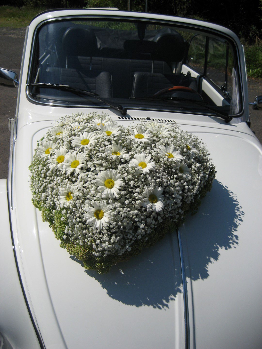 Das Bild zeigt ein Blumengesteck auf einem Hochzeitsauto