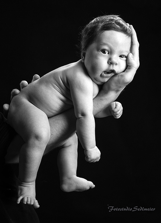 Das Bild zeigt ein schwarz-weiß Foto eines Babys, welches auf einem Arm gehalten wird
